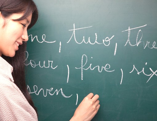 Professora anotando com giz branco no quadro os números em inglês