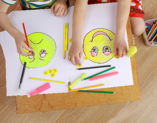 Crianças colorindo dois emojis, um feliz e um triste